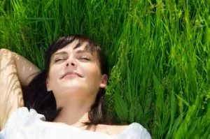 A woman relaxing in long grasses with closed eyes, not stressed about dental appointments.