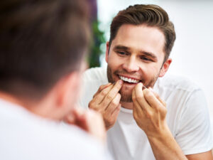 A young man flossing his teeth, preventing gum disease that may lead to tooth loss.