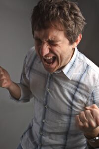 Person with clenched fists and open mouth, wearing a striped shirt, expressing intense pain.