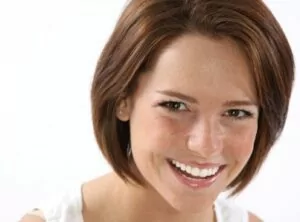 A woman with short brown hair smiles warmly, radiating joy and positivity in her expression.