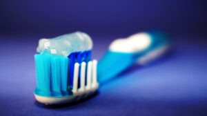 Close-up of a toothbrush with blue bristles and gel toothpaste on a blue background.
