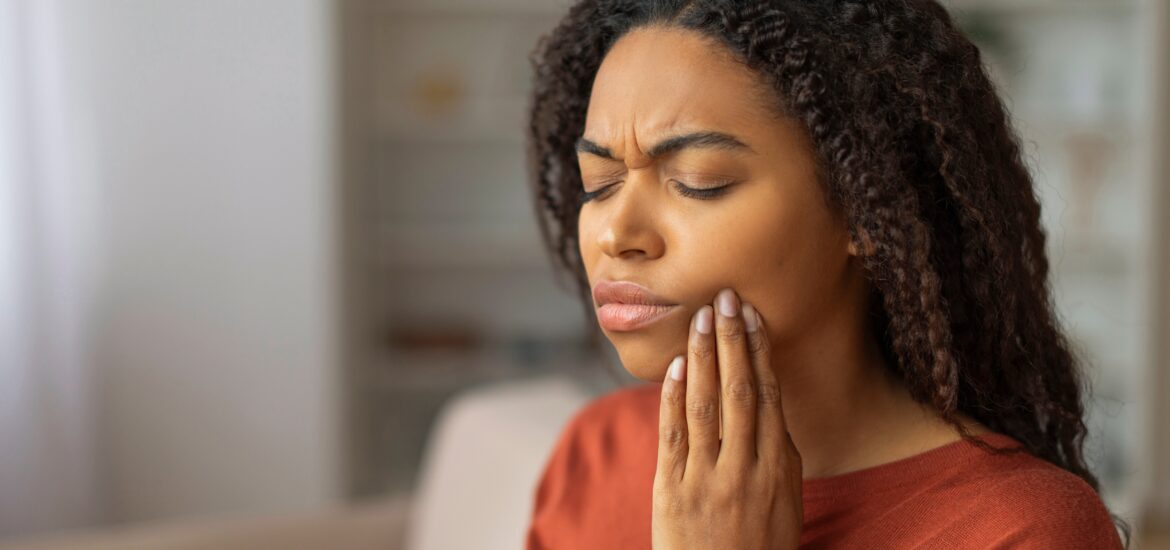 young woman in a red sweater holding her jaw, suffering from tooth pain