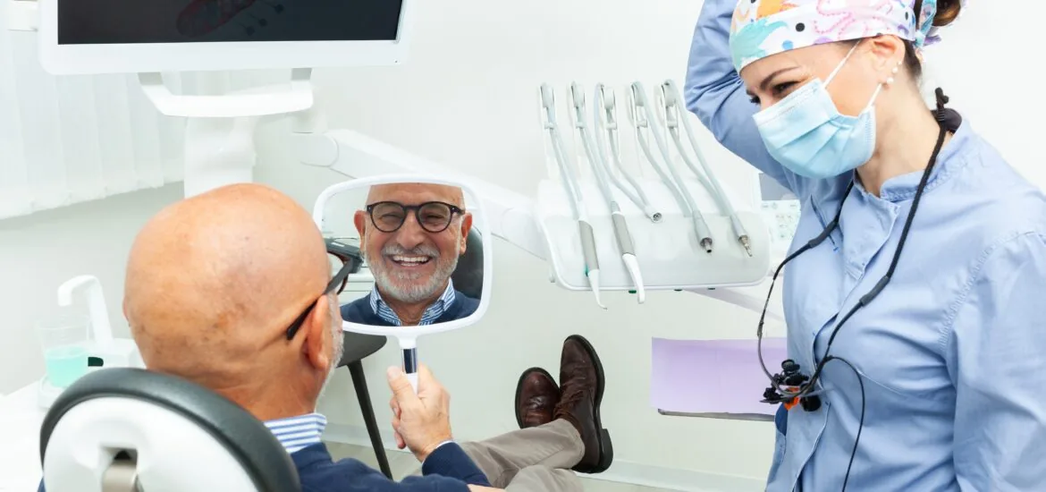 man smiling in a mirror, happy with his new dental implants