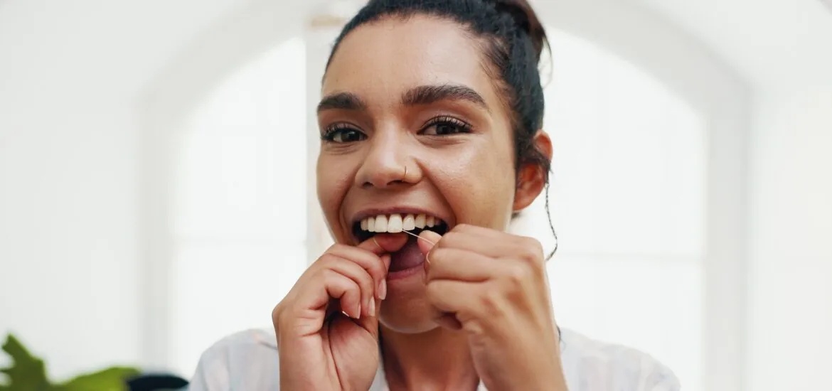 young woman flossing in a bathroom mirror, preventing gingivitis or gum disease